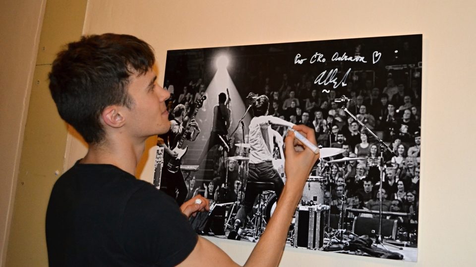 Albert Černý podepisuje fotografii Martina Straky, na které je zachycen ještě s kapelou Charlie Straight