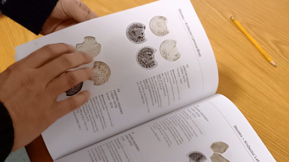 Listování v publickaci, která mapuje nález 98 stříbrných mincí