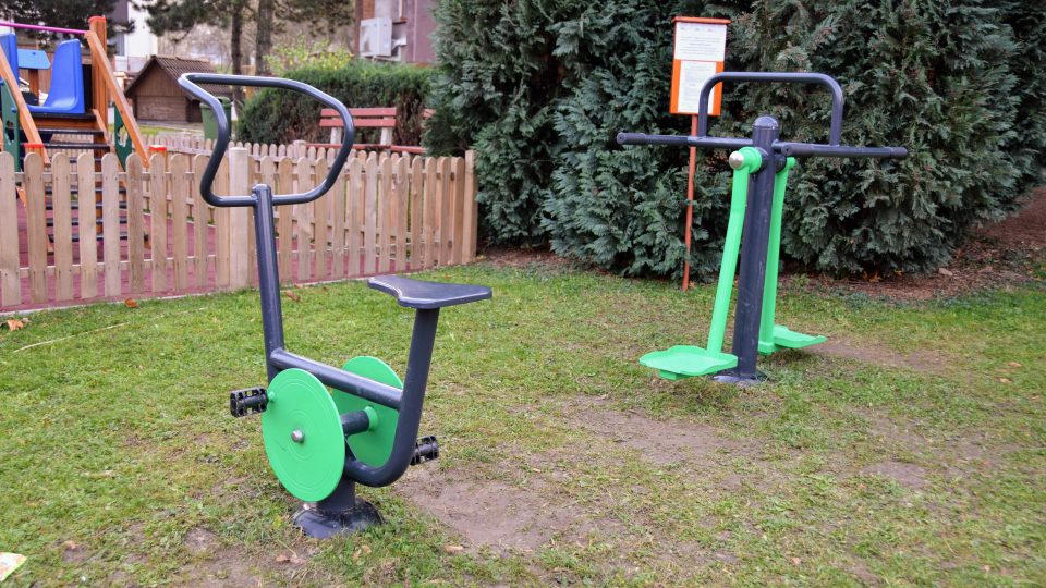 Dva stroje stojí u dětského hřiště před společenským domem